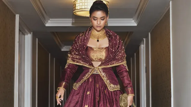 টেনে আঁচড়ানো স্লিক হাই বানে কীর্তির চুলে যোগ হয়েছে রাজকীয় ও পরিশীলিত ভাব।